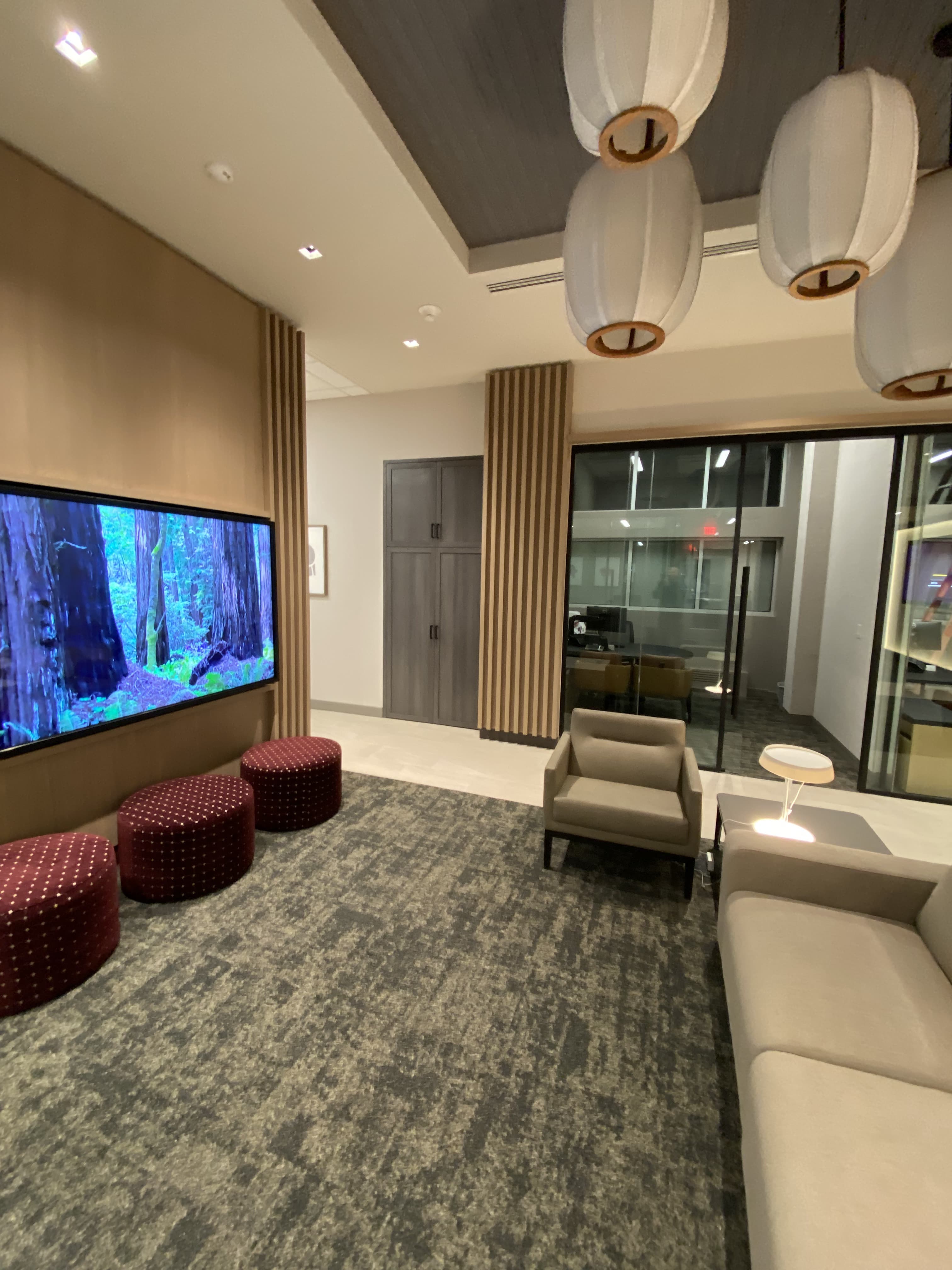 Finished commercial lounge with slatted media wall and lantern pendants by Deerfield Interiors